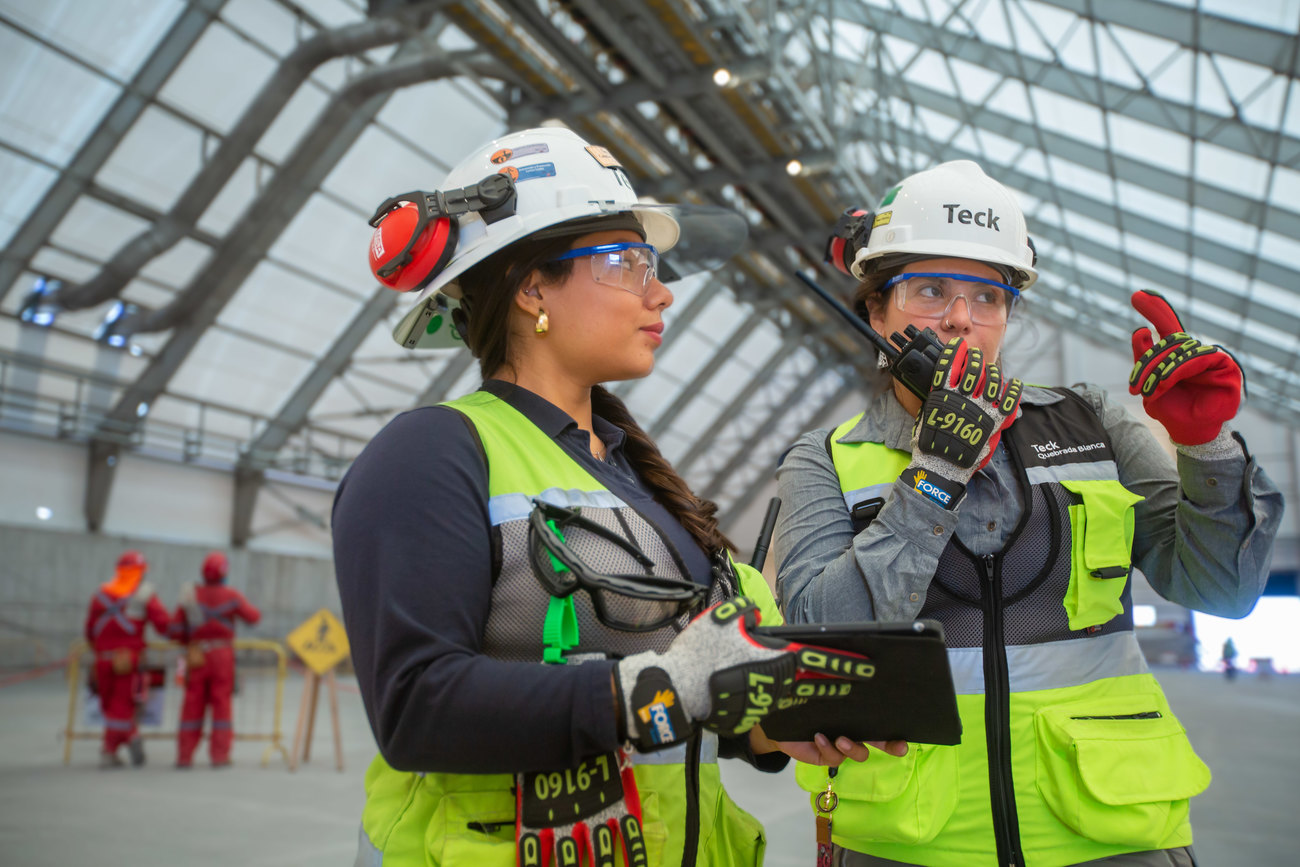 Two construction workers in protective gear discussing plans inside a large industrial facility.